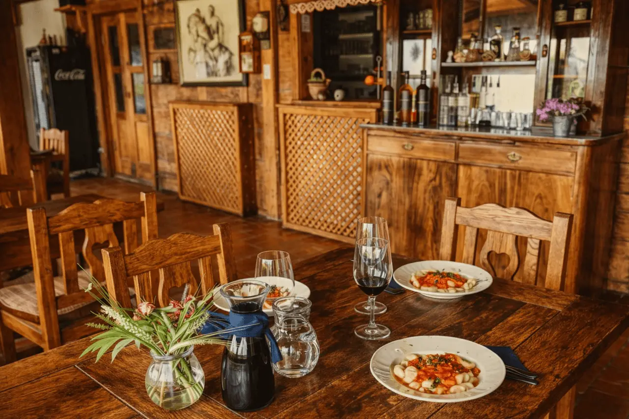 Rustikalni interijer restorana — drveni stolovi, sunčanice i pogled na zelenilo